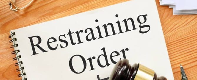 A judge gavel sits on top of a paper with the word restraining order