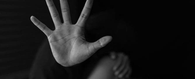 A grayscale image of a person holding up their hand as if to signal stop or to obscure their face.