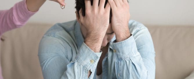 A person sits on the couch, clutching their head in distress over custody rights for grandparents, as another leans in, offering comfort with a ring in hand.