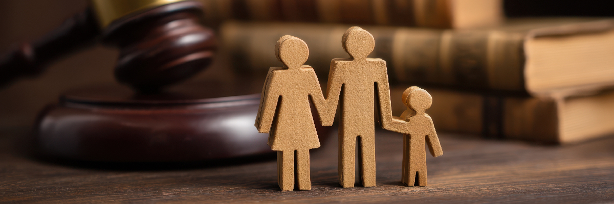 Family-Legal-Issues-in-California Wooden cutout figures of two adults and a child stand beside a gavel and law books, symbolizing family legal issues California families may face.